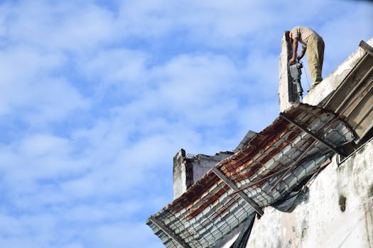 A construction worker using tools to demolish an old building roof against a sky background.